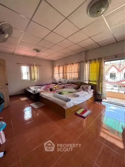 Spacious bedroom with large windows and balcony access, featuring cozy bedding and natural light.