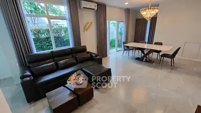 Spacious living room with elegant chandelier and garden view, featuring modern leather sofa and dining area.
