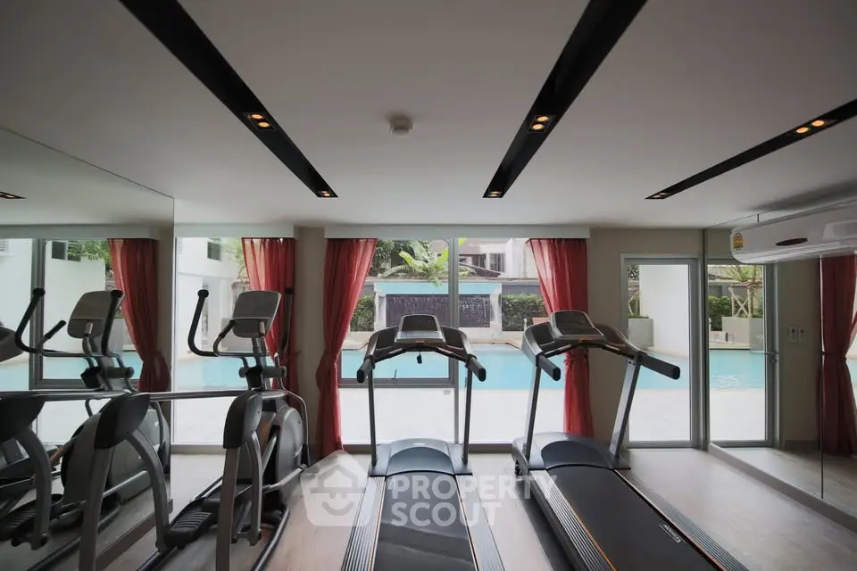 Modern gym with pool view featuring treadmills and exercise equipment in a luxurious setting.