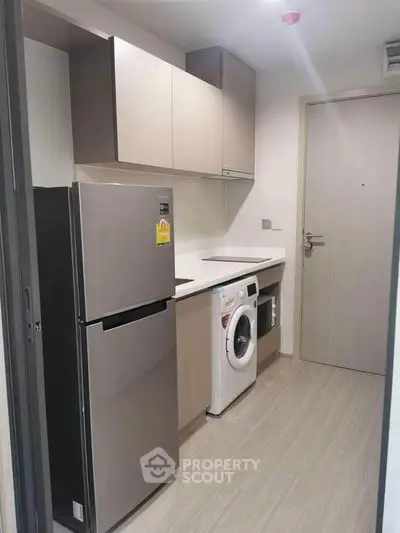 Modern kitchen with sleek appliances including fridge and washing machine in compact layout.