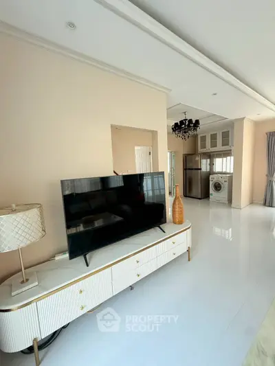 Modern living room with sleek TV, elegant decor, and open kitchen featuring stainless steel appliances.