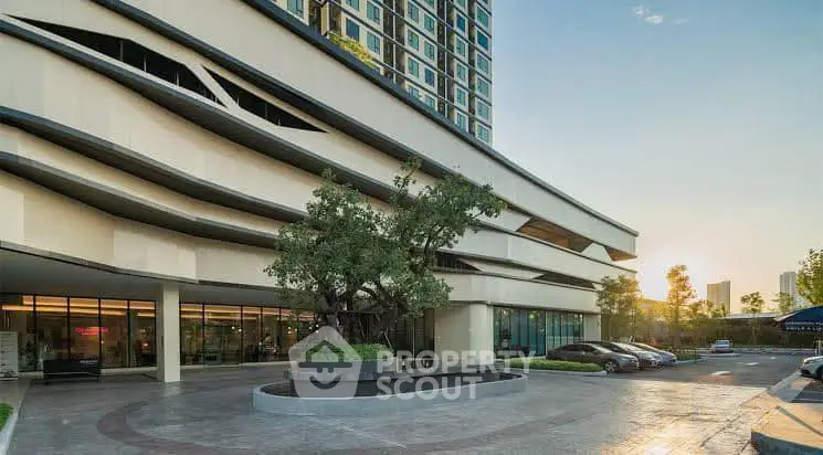 Modern building entrance with sleek design and luxury cars parked outside, showcasing urban elegance.