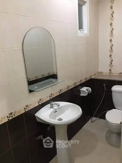 Modern bathroom with pedestal sink and toilet, featuring elegant tile design and wall-mounted mirror.