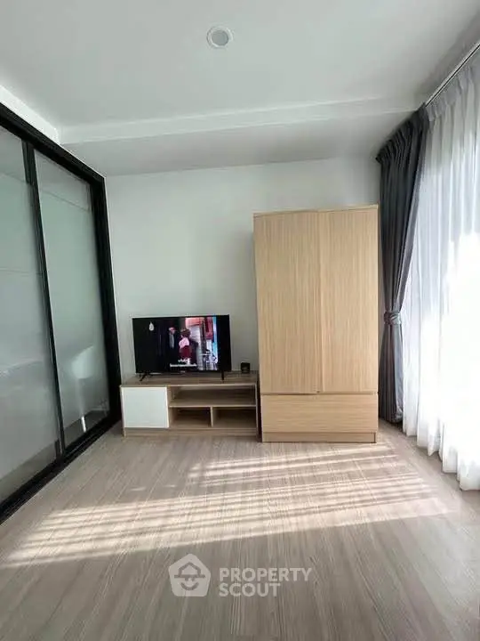 Bright modern living room with sleek TV stand and wardrobe, featuring large windows and elegant curtains.