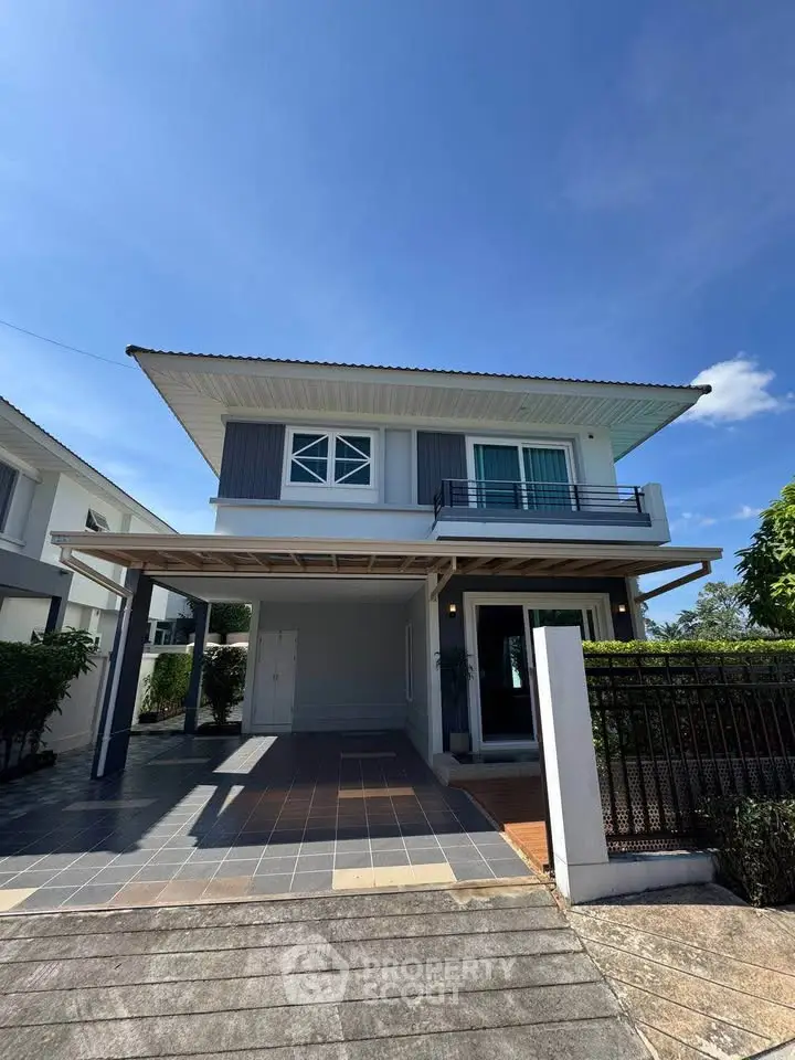 Modern two-story house with balcony and spacious driveway under clear blue sky.
