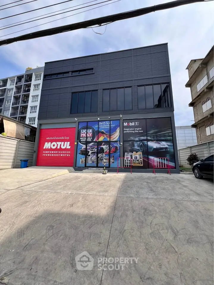 Modern commercial building with large glass windows and ample parking space, ideal for automotive businesses.