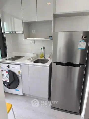 Compact modern kitchen with stainless steel fridge and washing machine in sleek apartment.