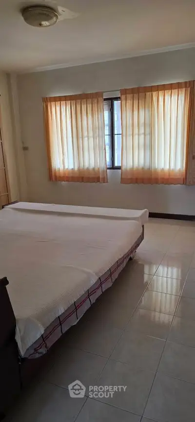 Spacious bedroom with natural light and tiled flooring in a cozy apartment.
