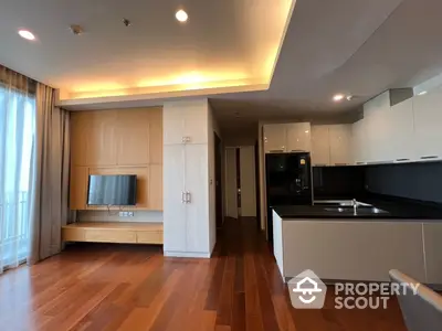 Spacious modern apartment with open layout kitchen featuring sleek cabinetry and built-in appliances, flowing into a cozy living area with hardwood floors and ample natural light.