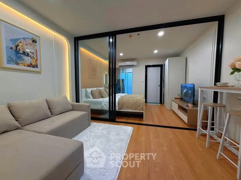 Modern studio apartment with cozy living area and stylish bedroom separated by glass partition.