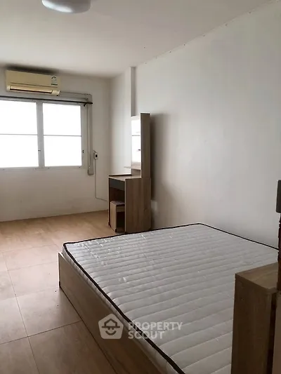 Minimalist bedroom with natural light and wooden flooring, featuring a bed and study desk.