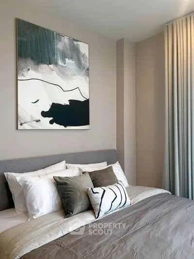 Modern bedroom with stylish decor and abstract art, featuring cozy bedding and elegant curtains.