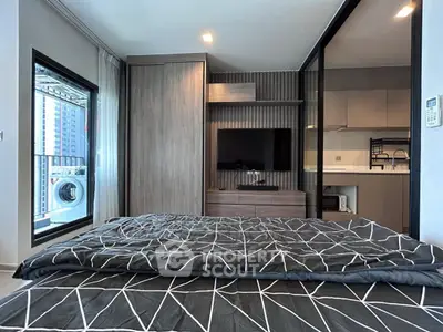 Modern bedroom with stylish decor and city view, featuring a sleek TV setup and adjacent kitchen area.