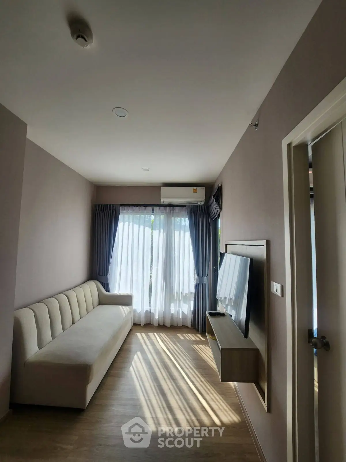 Modern living room with natural light, sleek sofa, and wall-mounted TV, perfect for relaxation.