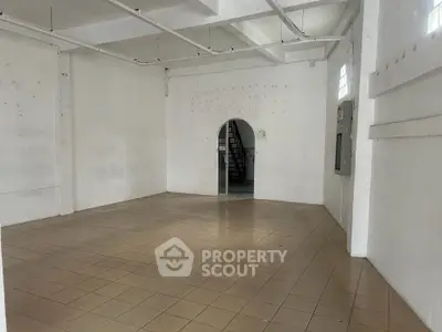 Spacious industrial-style room with tiled floor and arched doorway, ideal for creative workspace.