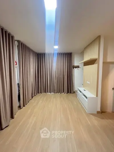 Spacious empty room with wooden flooring and modern curtains, ideal for versatile living space.