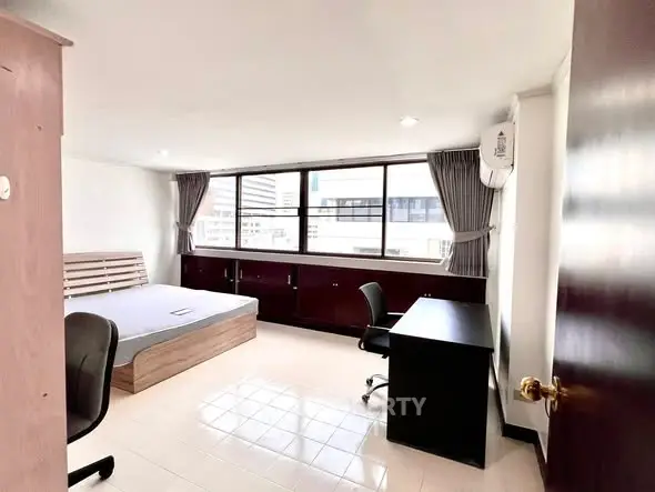 Spacious bedroom with large windows and modern furnishings in urban apartment.