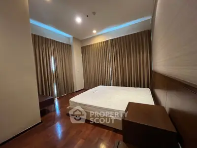 Spacious bedroom with wooden flooring and large windows, featuring elegant curtains and modern lighting.