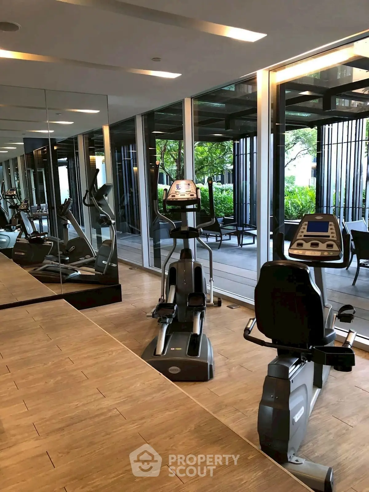 Modern gym with exercise equipment and large windows overlooking greenery.