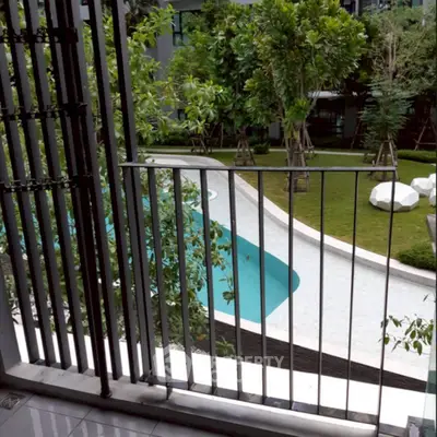 Charming balcony view overlooking lush garden and inviting pool in modern residential complex.