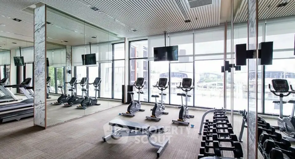 Spacious modern gym with state-of-the-art equipment and large windows offering natural light.