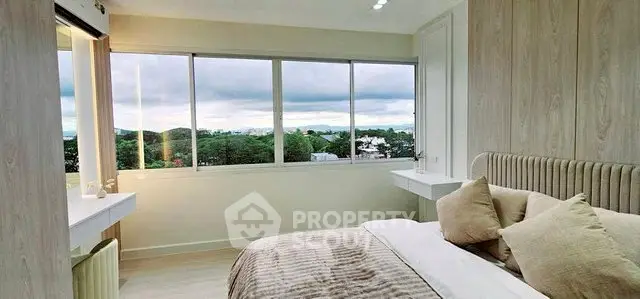 Bright bedroom with large windows offering stunning views of lush greenery.