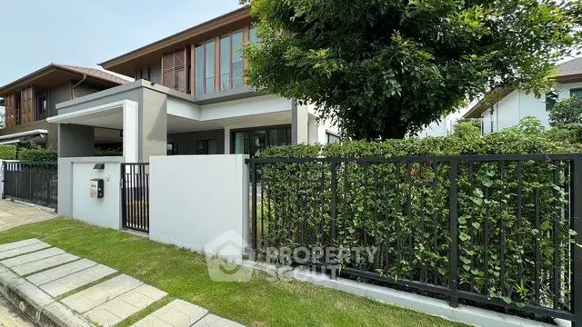 Modern two-story house with lush garden and sleek fence in a serene neighborhood.