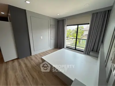 Spacious bedroom with large window and modern design, featuring wooden flooring and ample natural light.