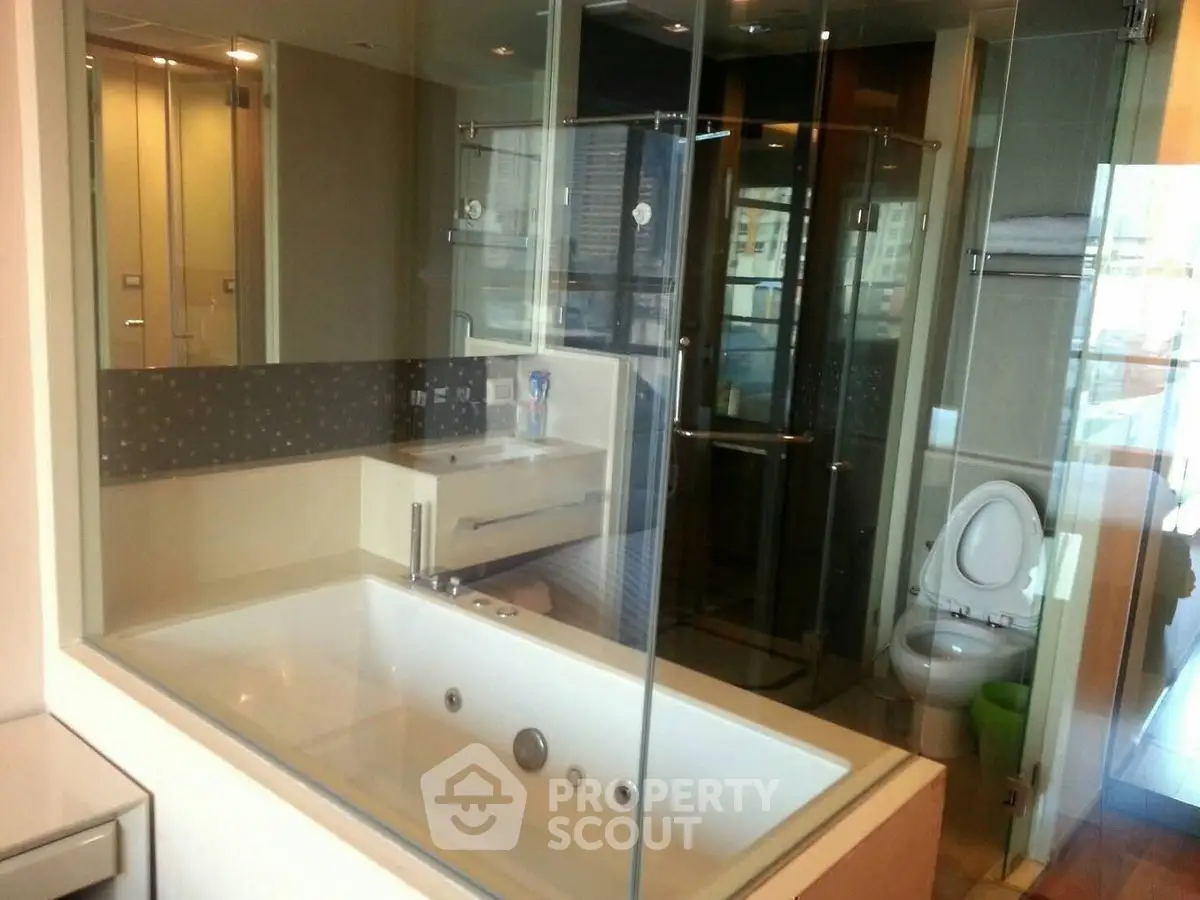Luxurious bathroom with glass shower and large bathtub in modern apartment.