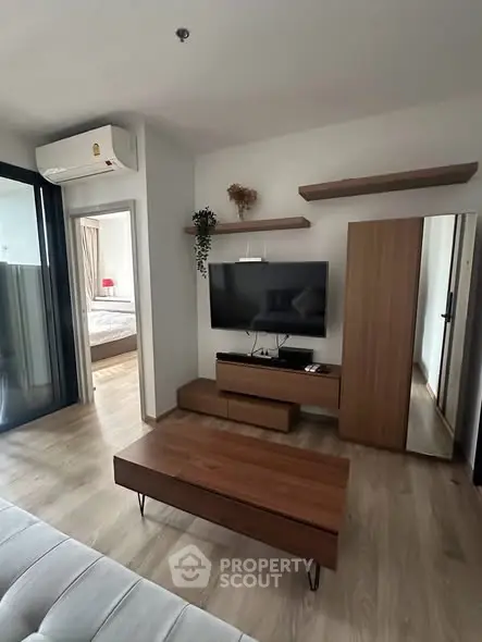 Modern living room with sleek wooden furniture and wall-mounted TV, adjacent to a cozy bedroom.
