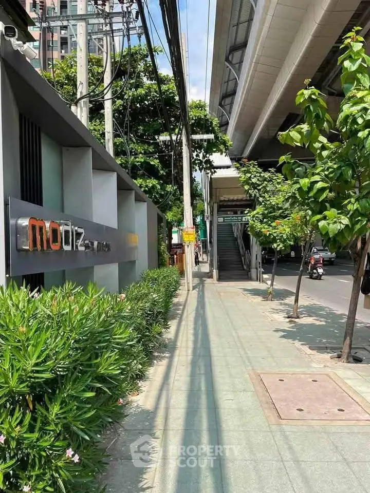 Modern urban sidewalk near residential building with lush greenery and city infrastructure.