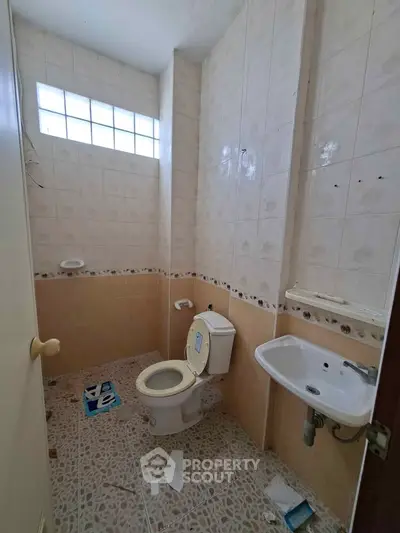 Compact bathroom with tiled walls and floor, featuring a toilet and sink.