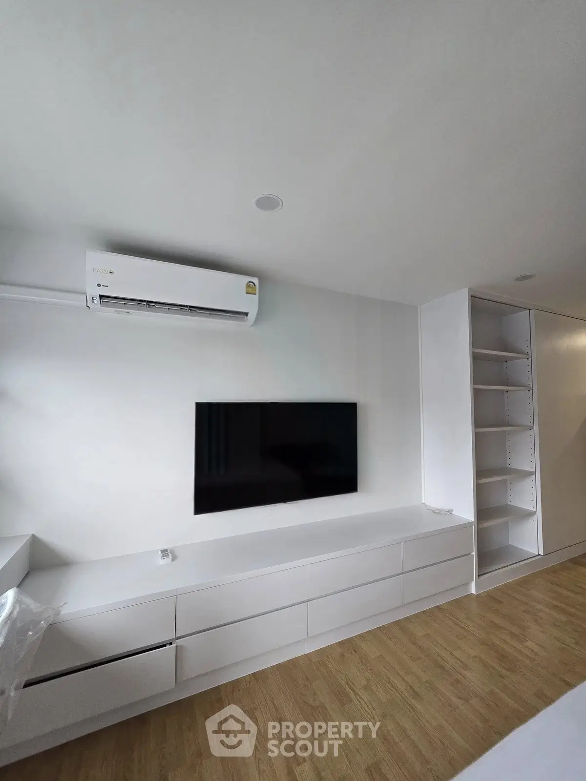 Modern living room with sleek white cabinetry and wall-mounted TV, featuring a minimalist design and air conditioning.