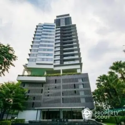 Modern high-rise building with contemporary design and lush greenery surroundings.