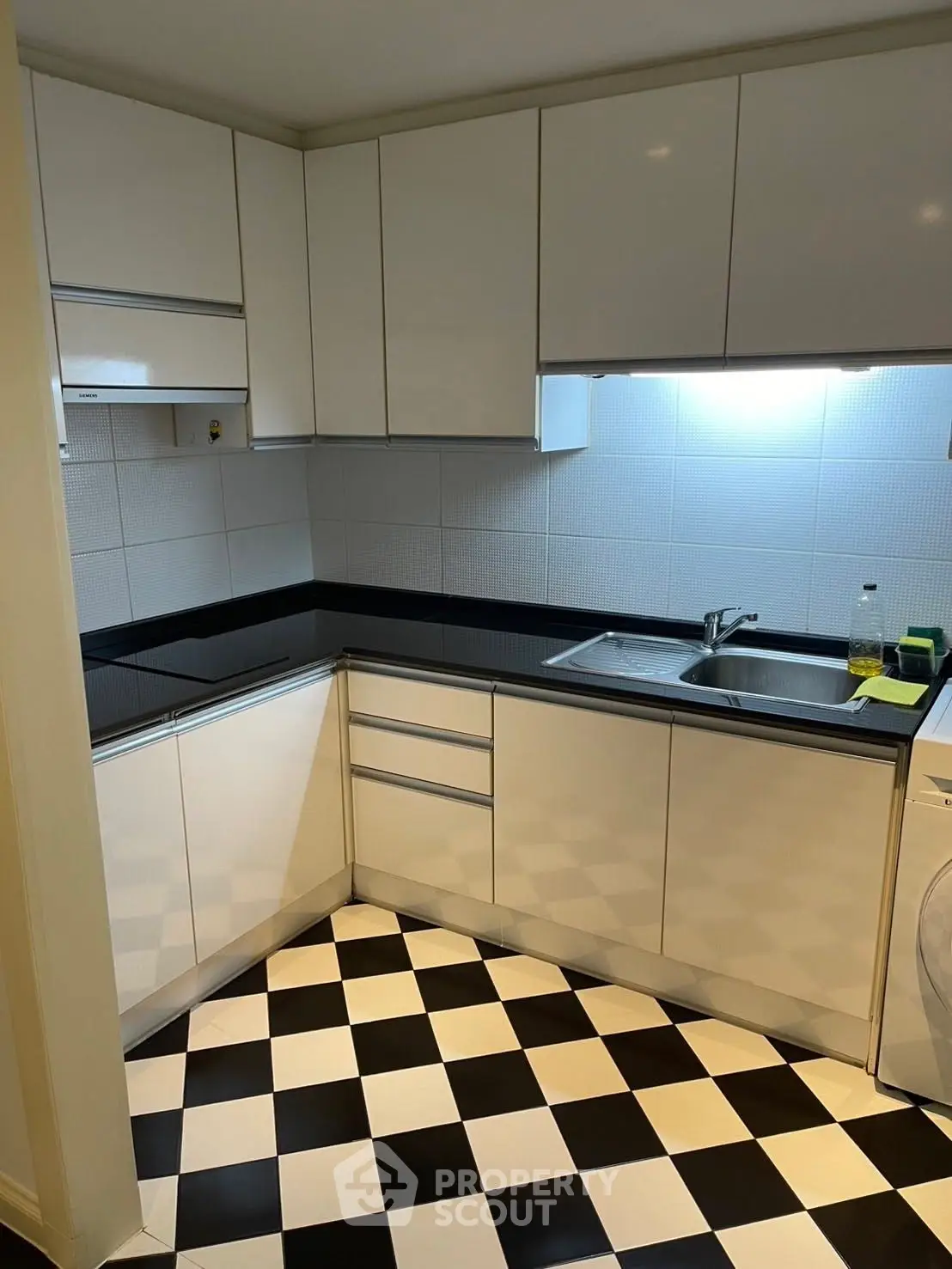 Modern kitchen with sleek white cabinets and black countertops, featuring a stylish checkered floor.