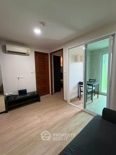 Modern living room with sliding glass doors leading to a cozy dining area, featuring sleek wooden flooring and air conditioning.