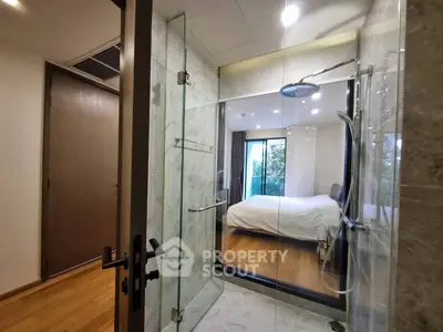 Modern bedroom with glass shower and wooden flooring, offering a sleek and contemporary design.