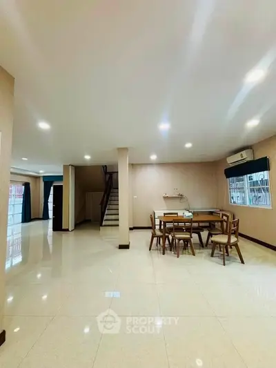 Spacious open-plan living area with dining set and staircase, featuring bright tiled flooring and modern lighting.