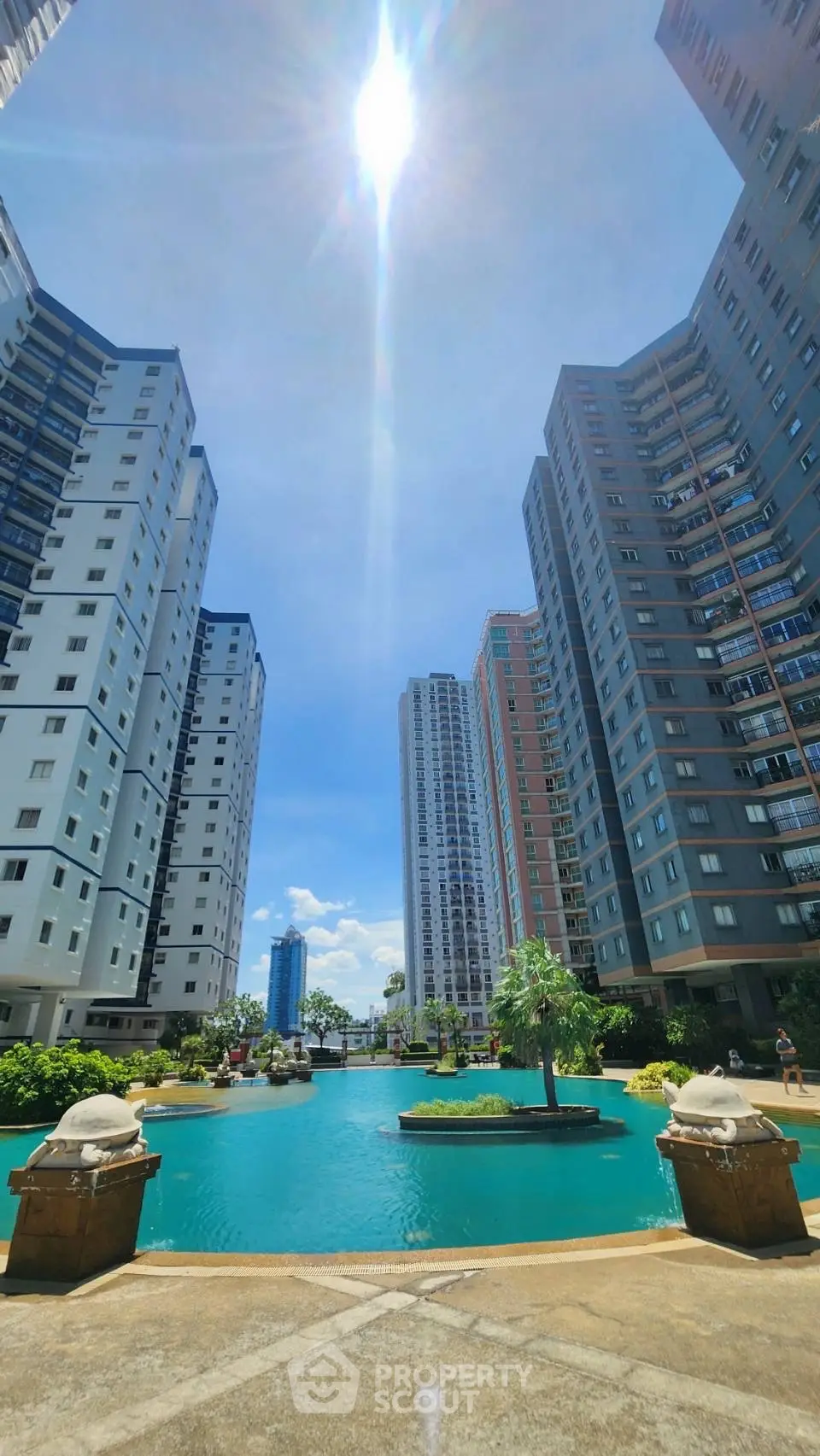 Stunning view of modern high-rise buildings surrounding a serene pool under a bright blue sky.