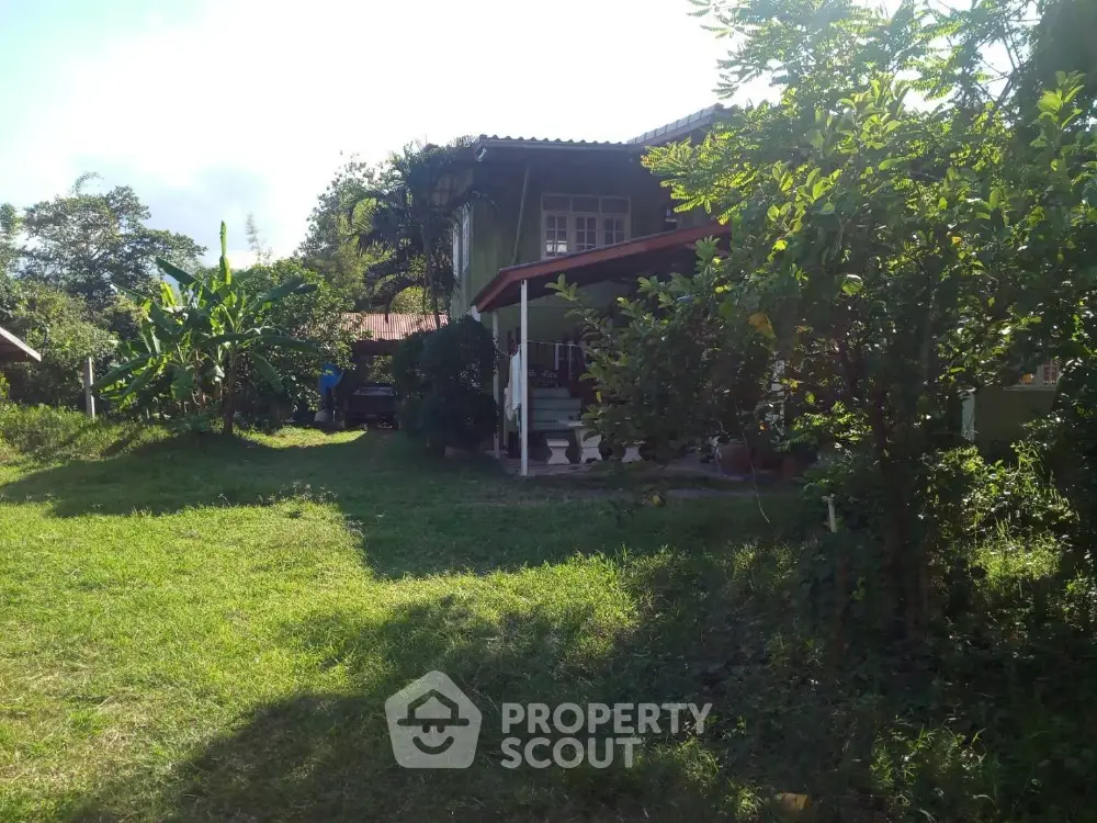 Charming two-story home nestled in lush greenery with a spacious lawn and inviting red-trimmed porch, offering a serene escape in a tranquil neighborhood.