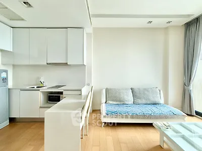 Modern minimalist kitchen and living area with sleek white cabinetry and cozy sofa.