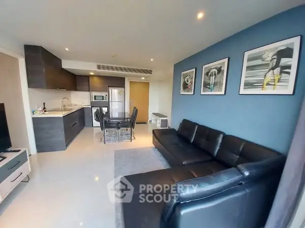 Modern living room with sleek black leather sofas and stylish kitchen area.