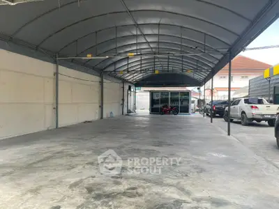 Spacious covered parking area with multiple vehicles and a small office building in the background.
