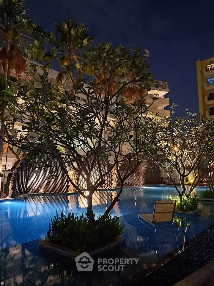 Luxurious night view of a serene pool surrounded by lush greenery and modern architecture.