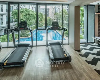 Modern gym with treadmills overlooking a luxurious pool and garden view.