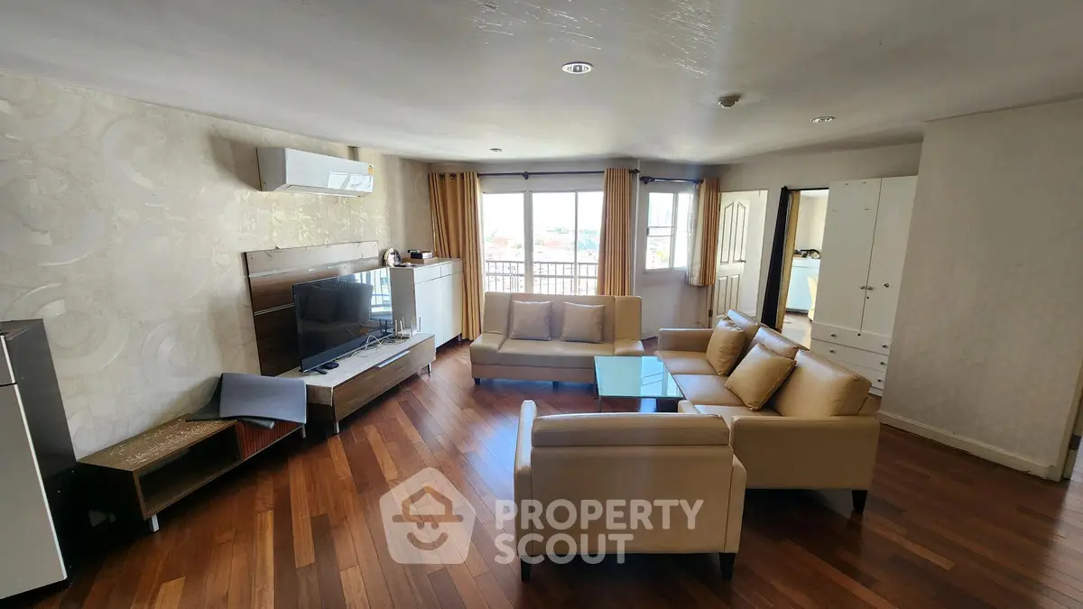 Spacious living room with modern furniture and wooden flooring, featuring a large window with a view.