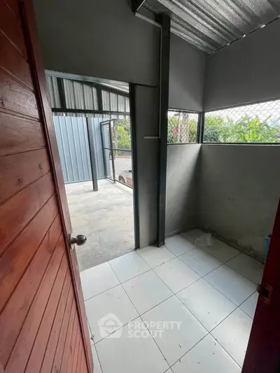 Compact storage room with tiled floor and metal roof, leading to outdoor area.
