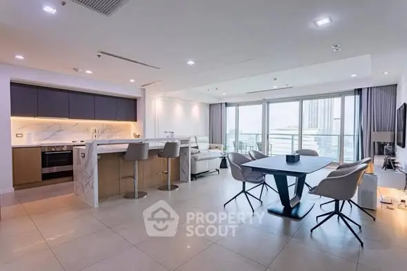 Spacious modern living room with open kitchen and large windows offering city views.