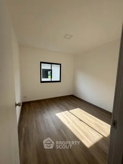 Spacious empty bedroom with wooden flooring and natural light through window.