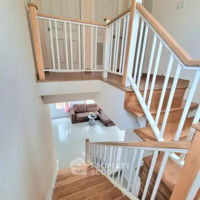 Elegant wooden staircase with white railings leading to a cozy living room.